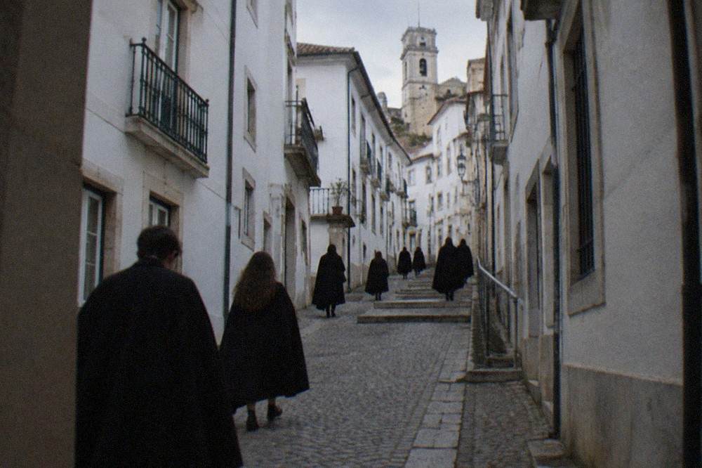 Students in black capes walking through a narrow cobbled street in Coimbra's upper town