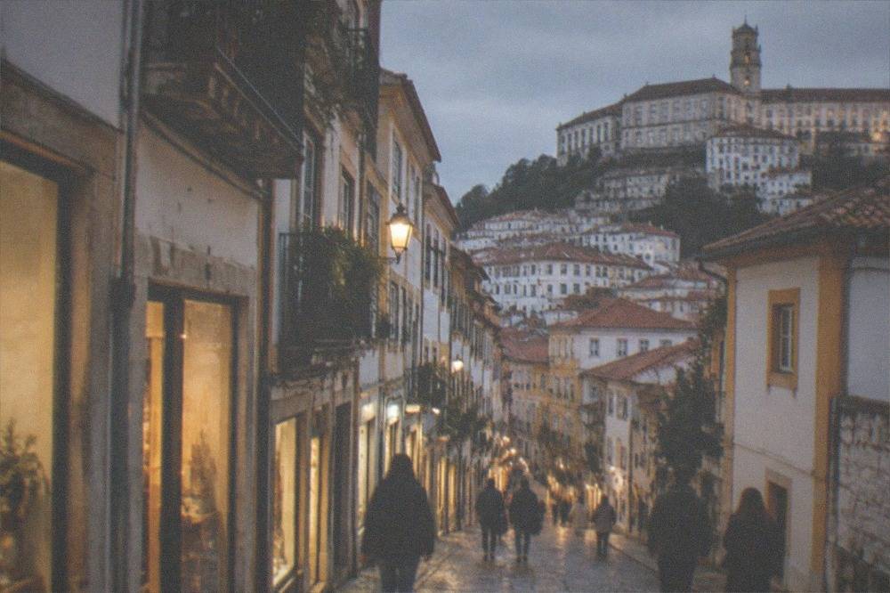An evening street in central Coimbra with lit shopfronts and people walking