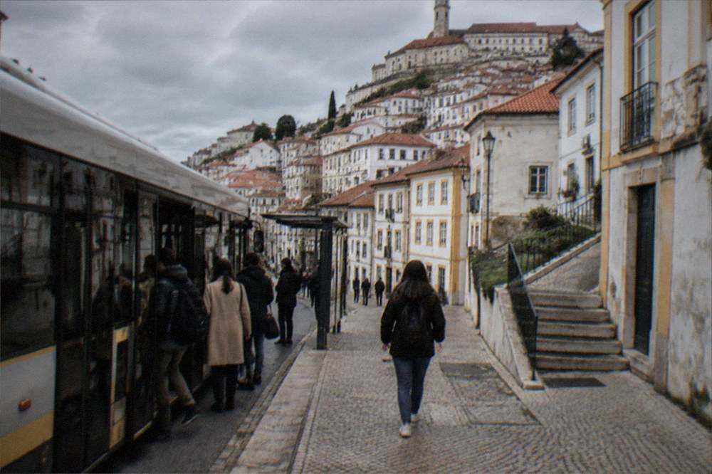 A city bus stopped at a street stop in central Coimbra with passengers boarding