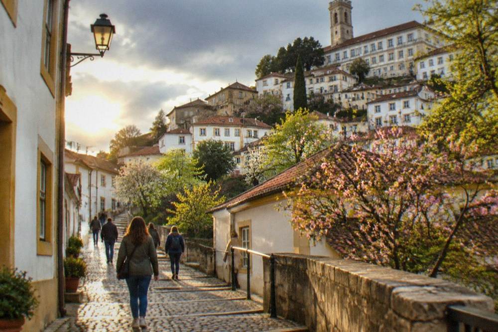 Visitors in light jackets walking up a cobbled street towards the university hill in Coimbra