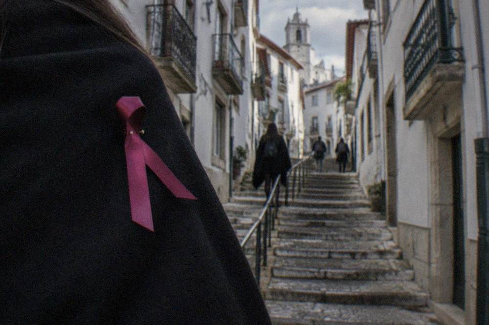 A close view of a student cape in black with a coloured ribbon pinned across the chest