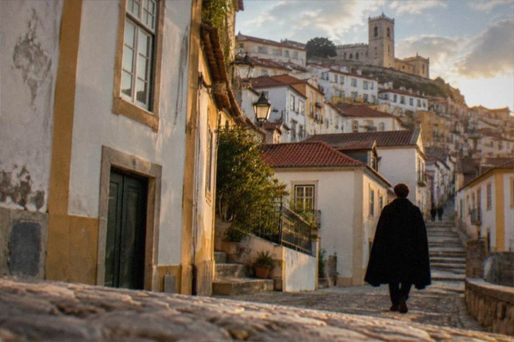 A quiet street in the Coimbra old town with a student in a black cape walking uphill