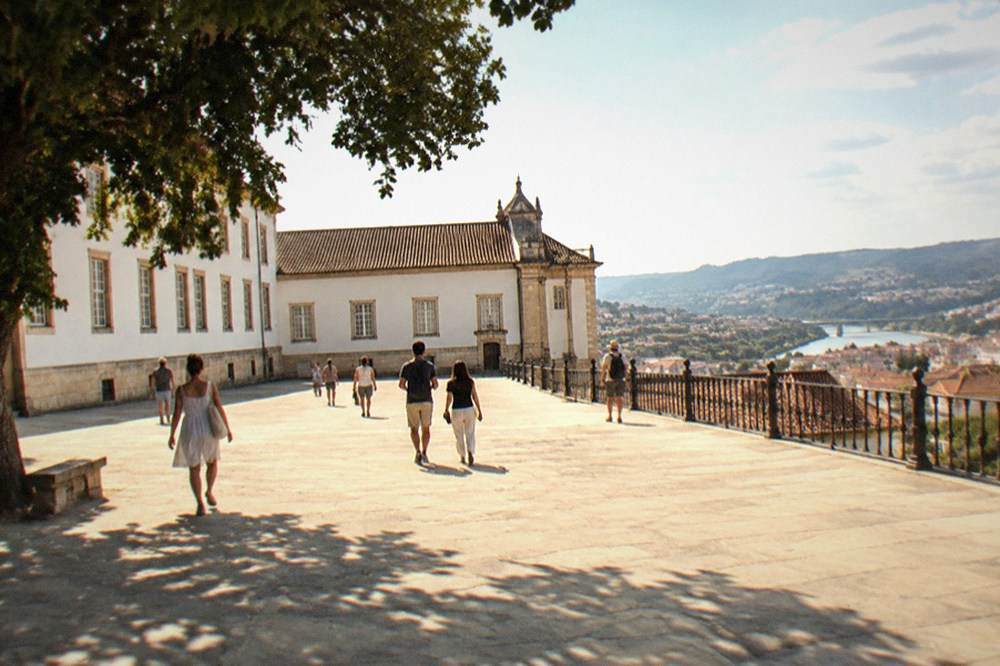 Visitors walking through the sunlit walled courtyard of the Paço das Escolas on the university hill