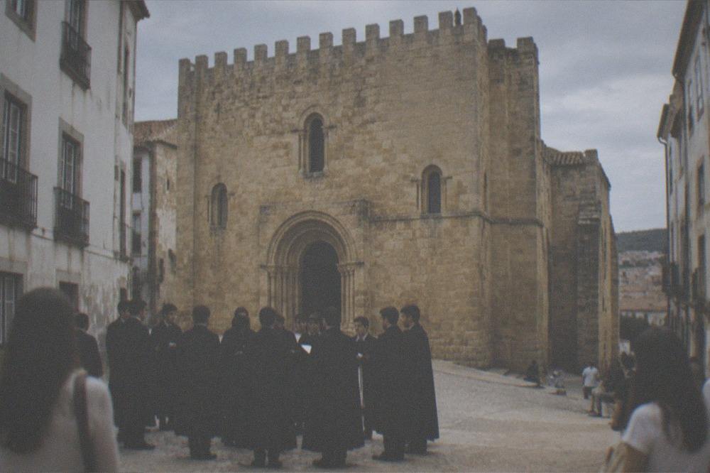 Students in black capes singing in the evening light outside the Sé Velha in Coimbra