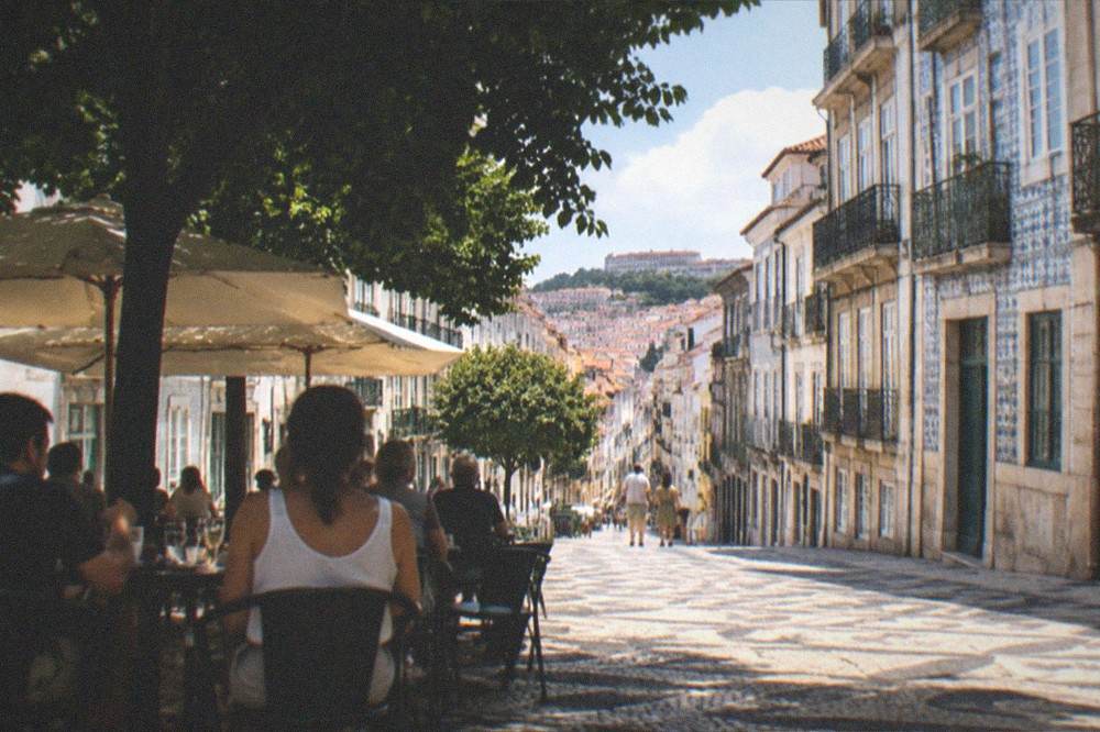 Diners at an outdoor table on a shaded square in Coimbra's Baixa in the evening