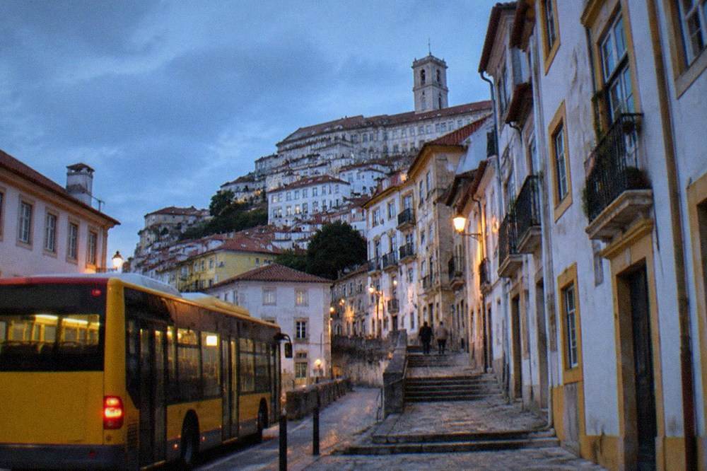 A yellow city bus stopped on a Coimbra street with old buildings behind