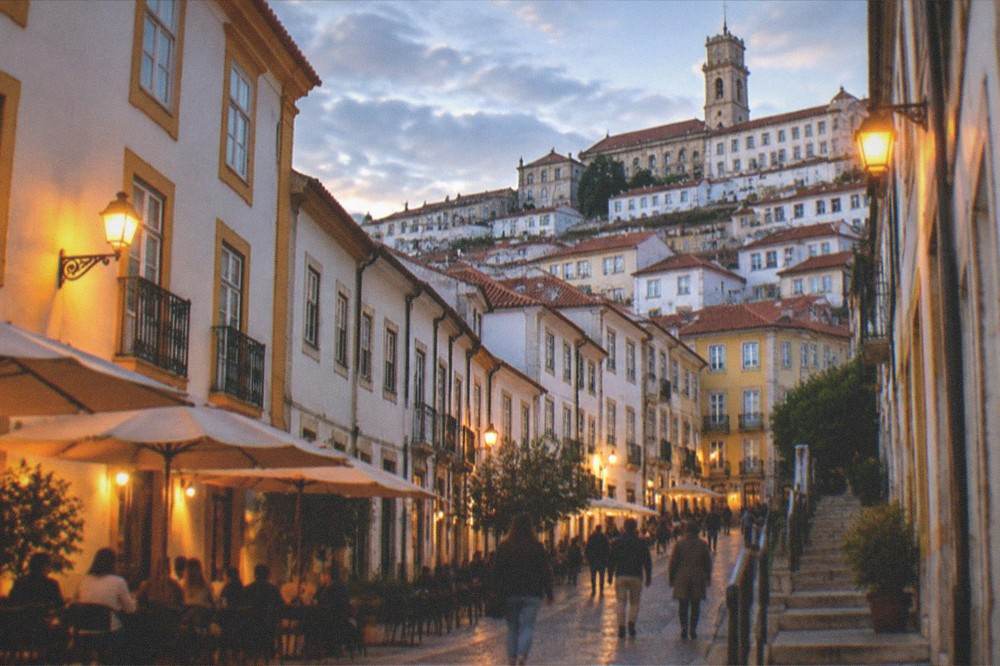 Evening view of a lit Coimbra street with people walking and café tables outside