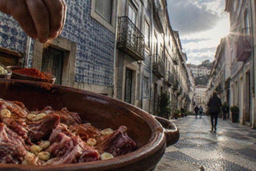 Pieces of raw goat meat being seasoned with garlic and paprika in a clay pot before cooking