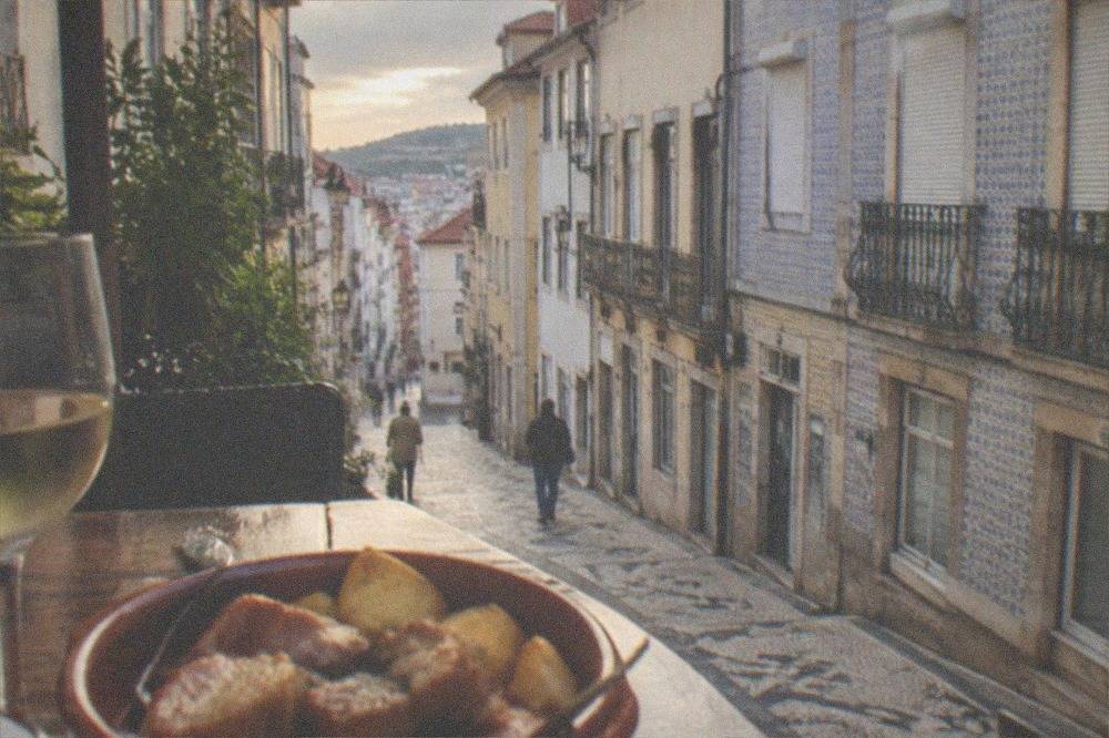 A rustic plate of pork rojões with fried potatoes and a glass of white wine on a café table