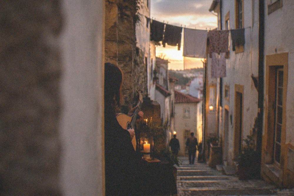 A fado singer in a black cape performing by candlelight with a Portuguese guitar