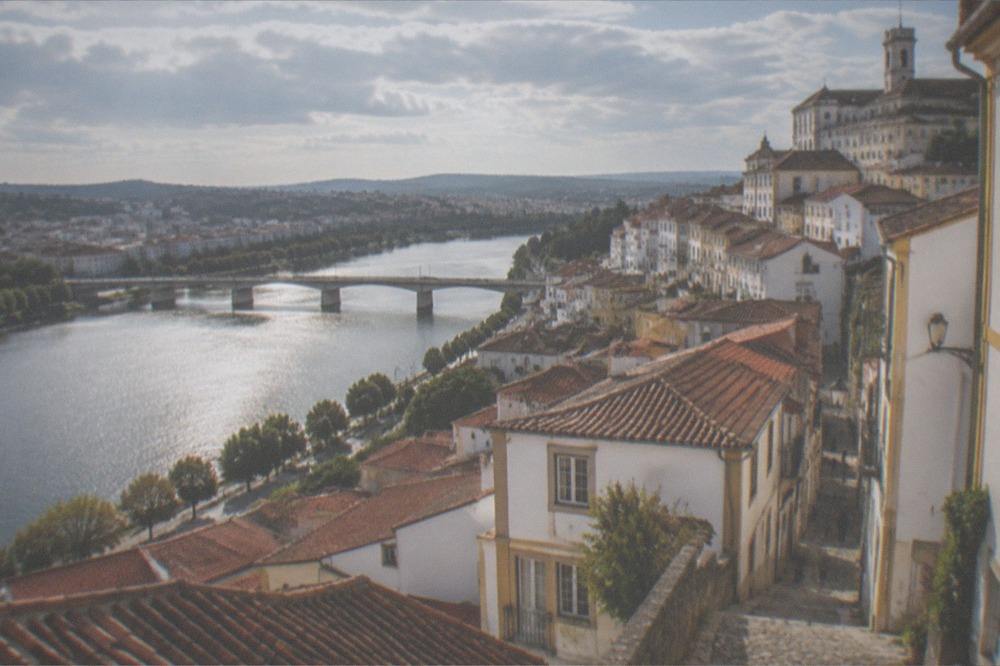 Red-roofed houses in Coimbra seen from above, with the River Mondego running through the city