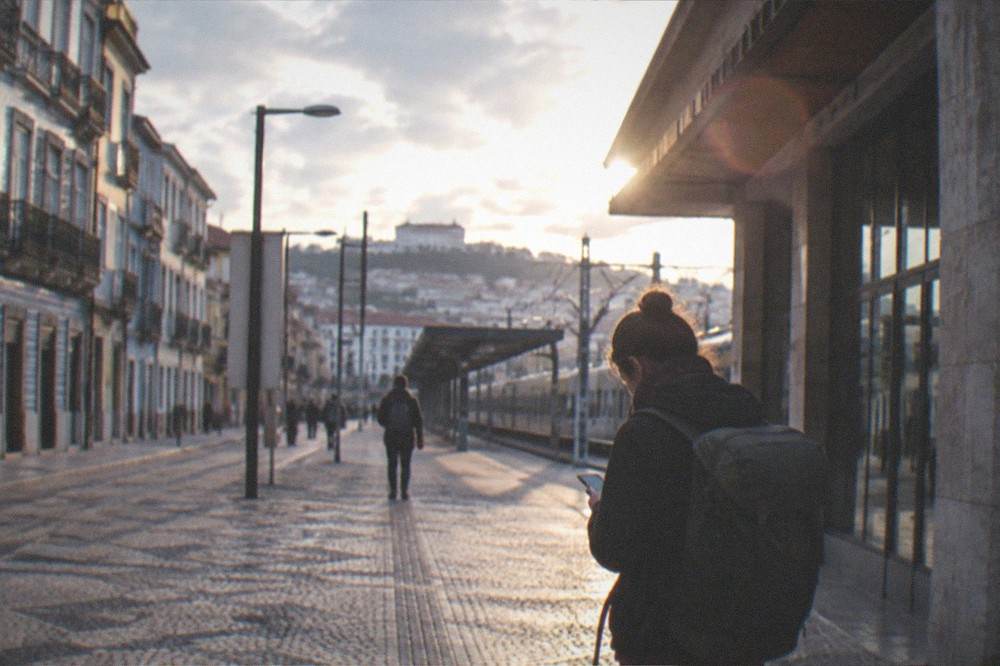 A traveller with a backpack consulting a phone outside a railway station in Portugal