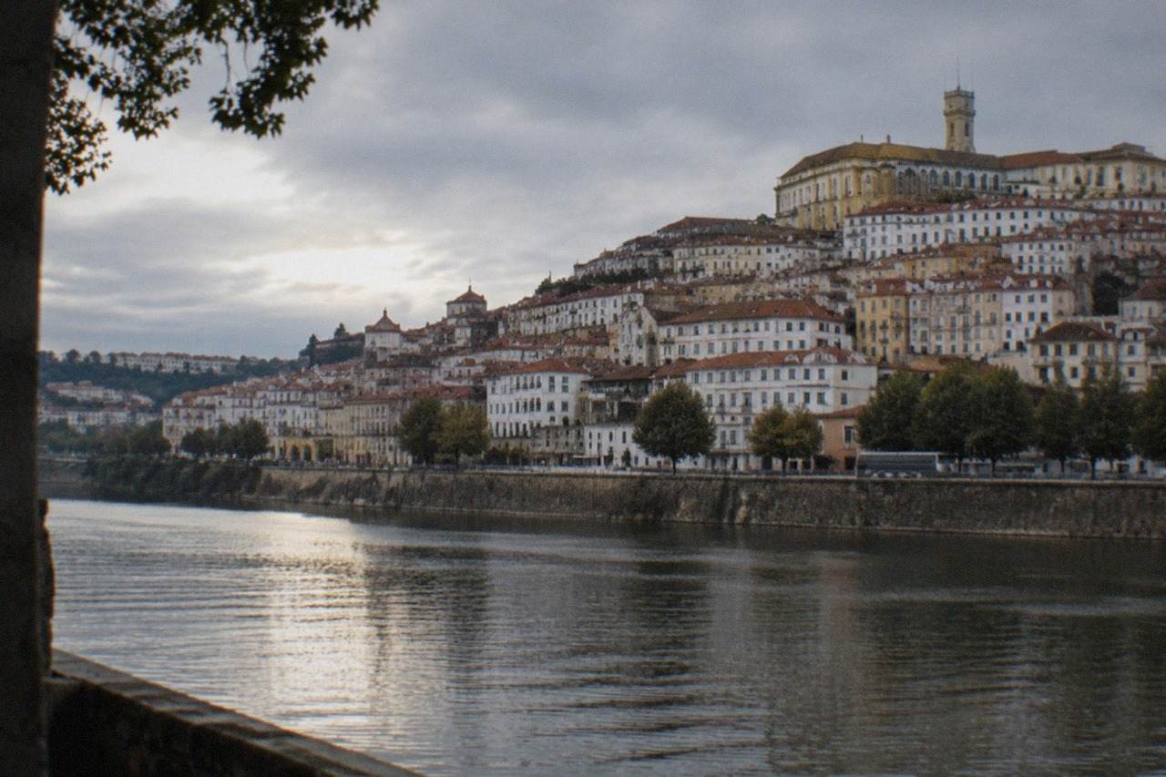 The hillside old town of Coimbra seen from across the River Mondego, with the university tower rising above tiled rooftops.