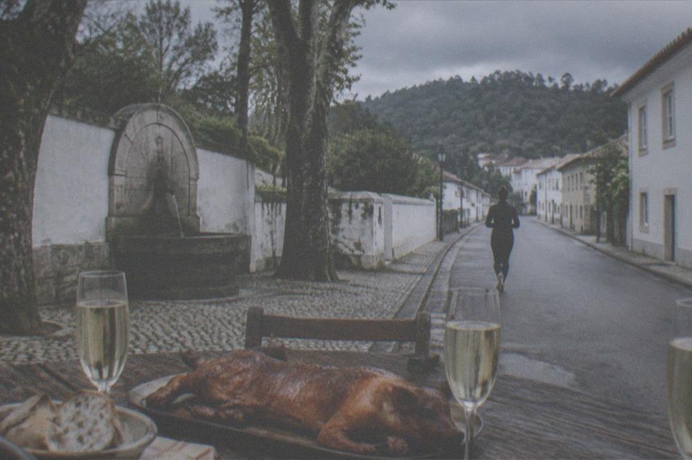A rustic table with roasted suckling pig, bread and glasses of sparkling wine.