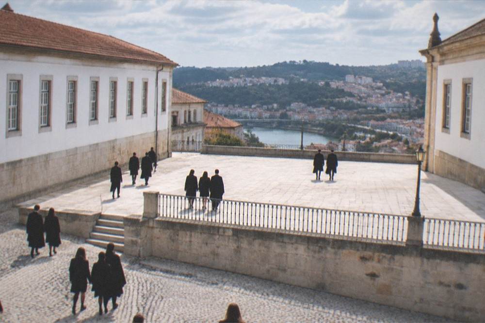 Students in black academic capes crossing a cobbled square below the university buildings