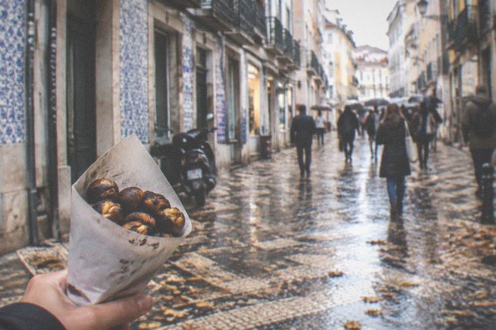 A bowl of roasted chestnuts in a paper cone on an autumn street