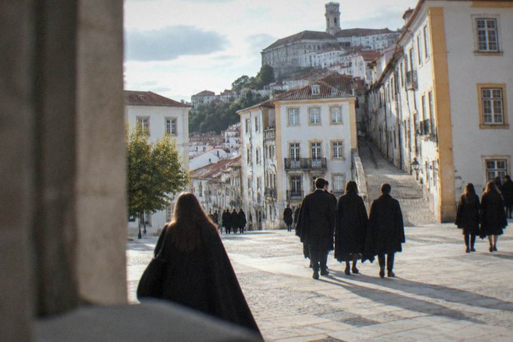 Students in black capes crossing a sunny square in Coimbra during May