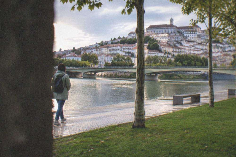 A traveller with a light rain jacket walking beside the Mondego river in Coimbra