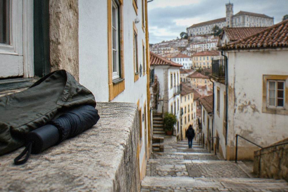 A light rain jacket and a compact umbrella folded on a stone windowsill