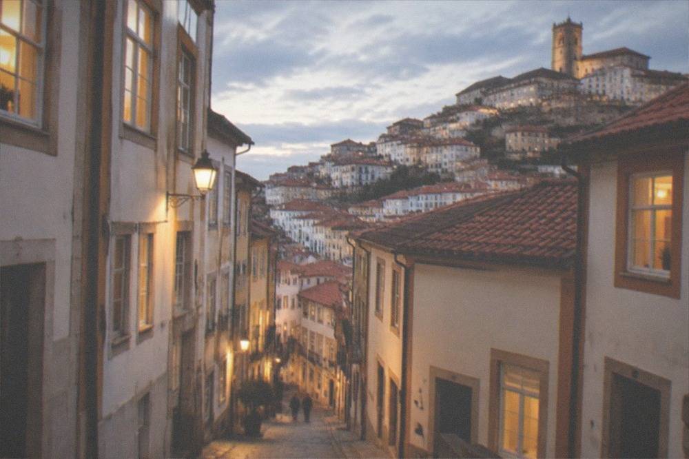 A narrow evening street in central Coimbra with lit windows above stone walls
