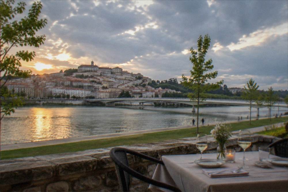 A table set for dinner on a stone terrace overlooking the Mondego river at dusk