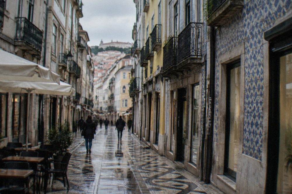 Narrow commercial street in downtown Coimbra with shopfronts and cafe tables
