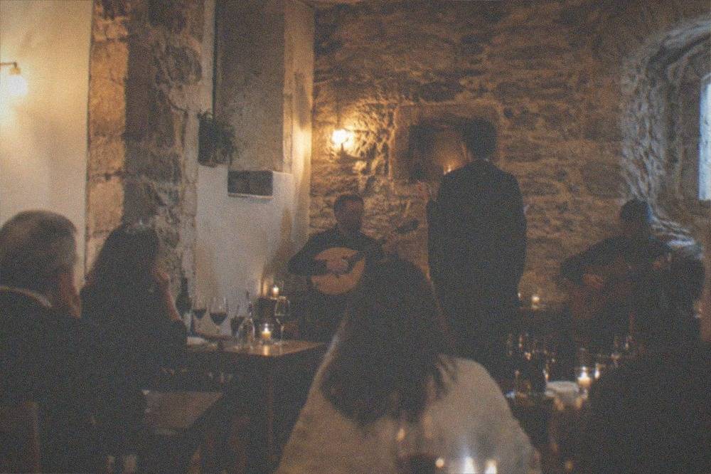 A singer performing fado in a small stone-walled room while diners listen with glasses of wine