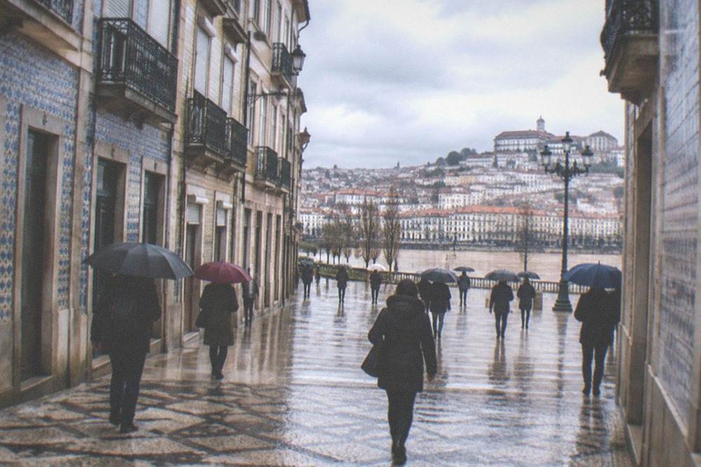 Visitors with umbrellas crossing the Praça do Comércio in Coimbra's downtown on a grey afternoon