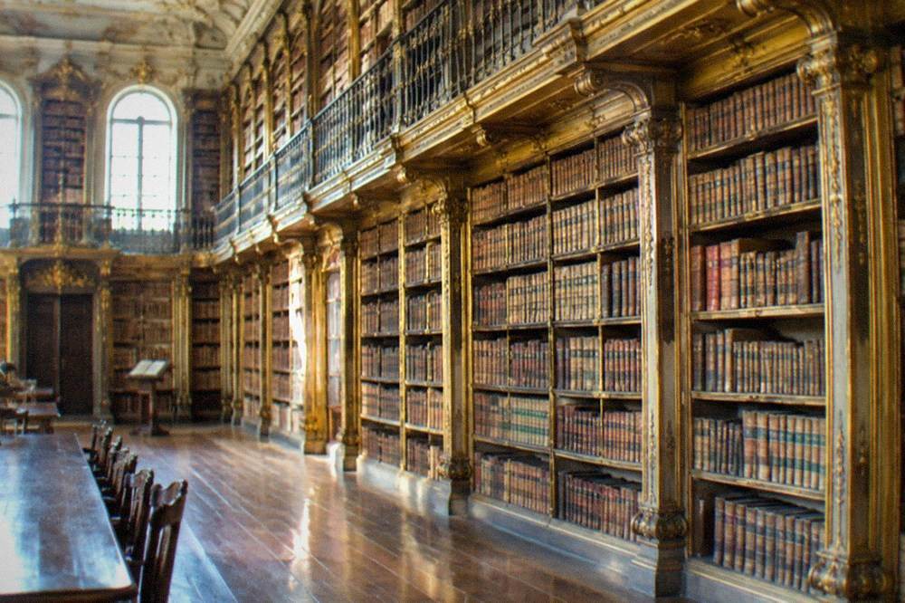 The baroque interior of a library hall with gilded bookshelves rising two storeys