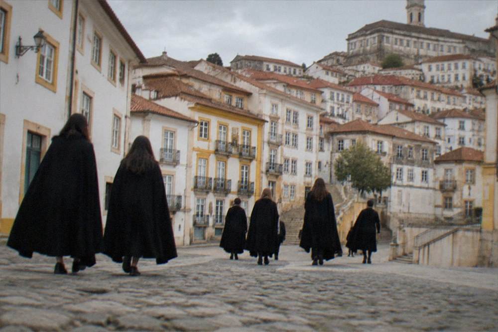 Students in traditional black capes crossing a cobbled square in Coimbra