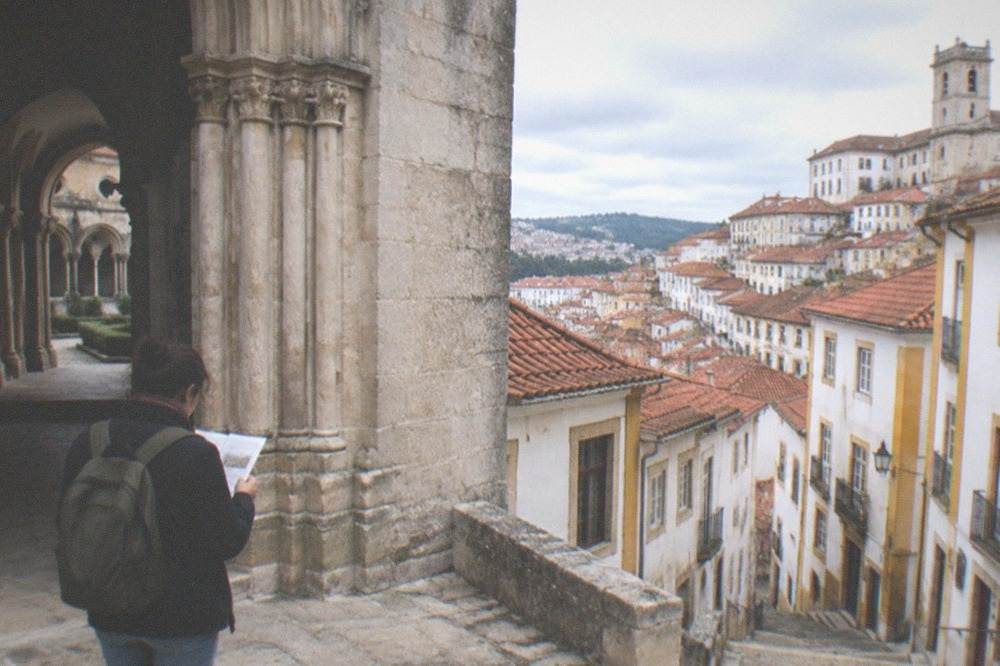 A visitor reading a ticket at the entrance of a stone monastery cloister in Coimbra