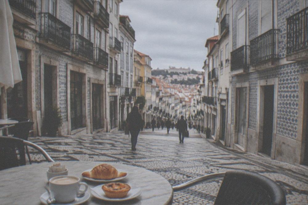 An outdoor cafe table with coffee and pastries on a cobbled square in Coimbra's lower town