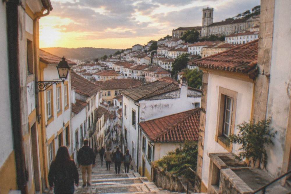 Visitors walking down a stone stairway alley between old buildings in Coimbra