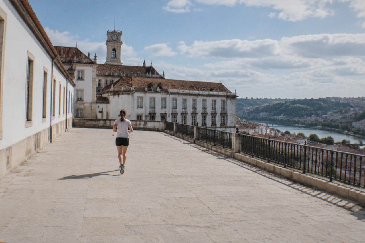 The University of Coimbra tower and palace buildings seen from the city below on a bright morning.