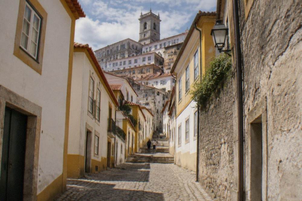 A narrow cobbled lane in Coimbra's old town with stone walls and warm afternoon light.