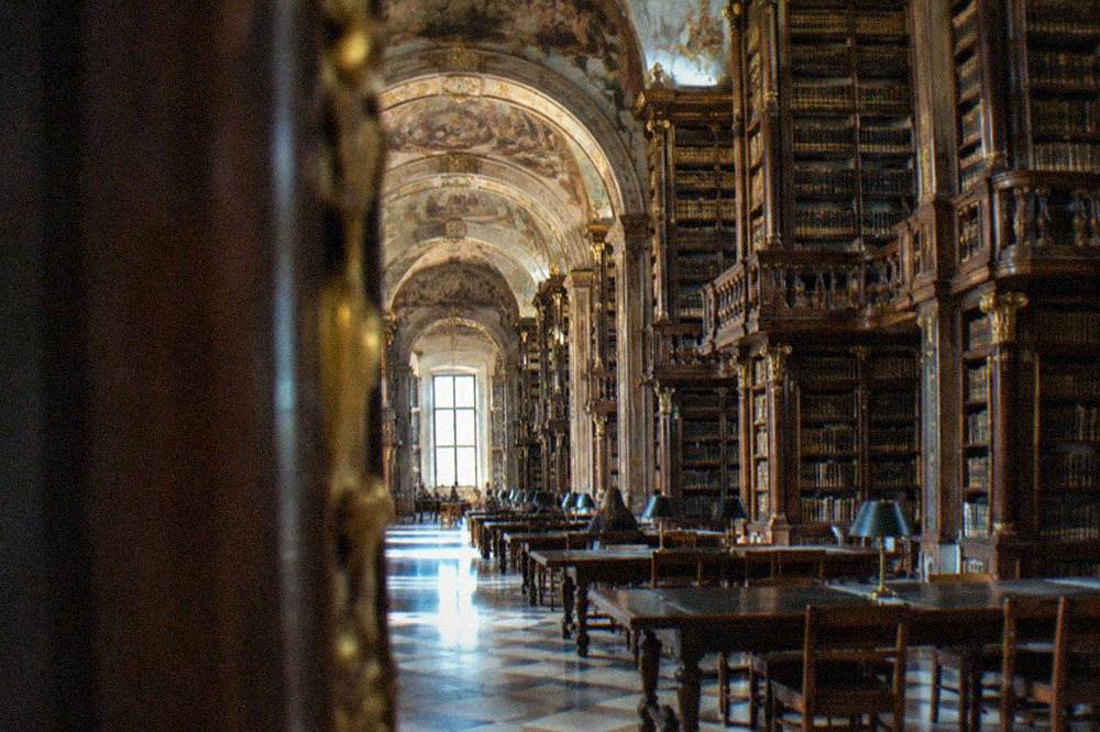 The baroque interior of the Biblioteca Joanina with tall wooden bookshelves and painted ceilings.