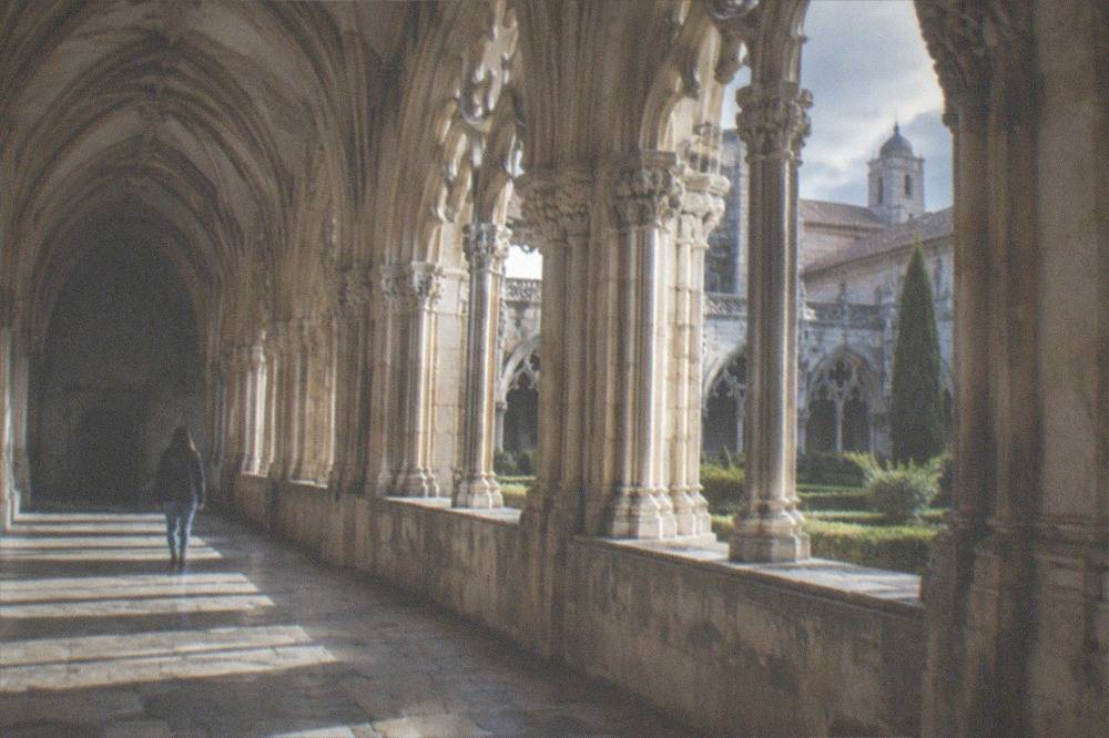 The stone cloister of a Coimbra monastery with sunlight falling across carved arches.