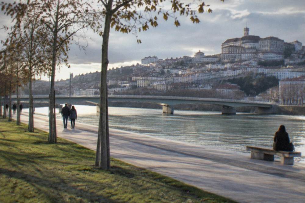 The wide walkway along the River Mondego with the city and its bridge in the background.