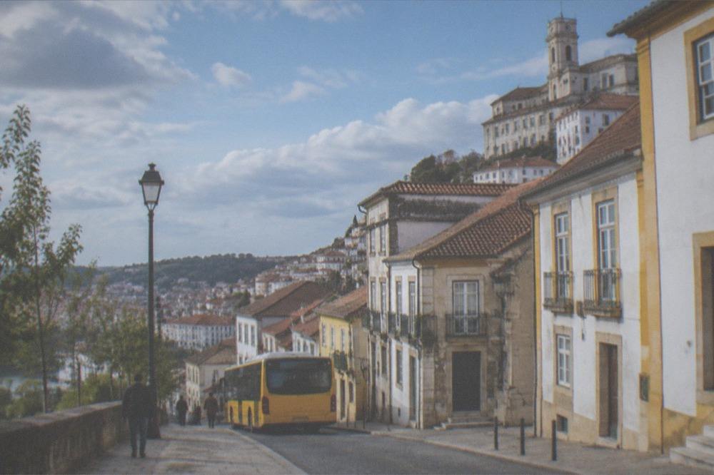 A yellow city bus stopped on a street in central Coimbra