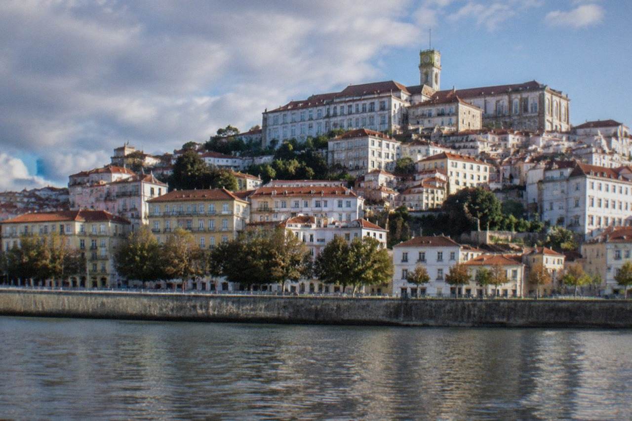 The old university buildings of Coimbra seen from across the River Mondego on a bright morning.