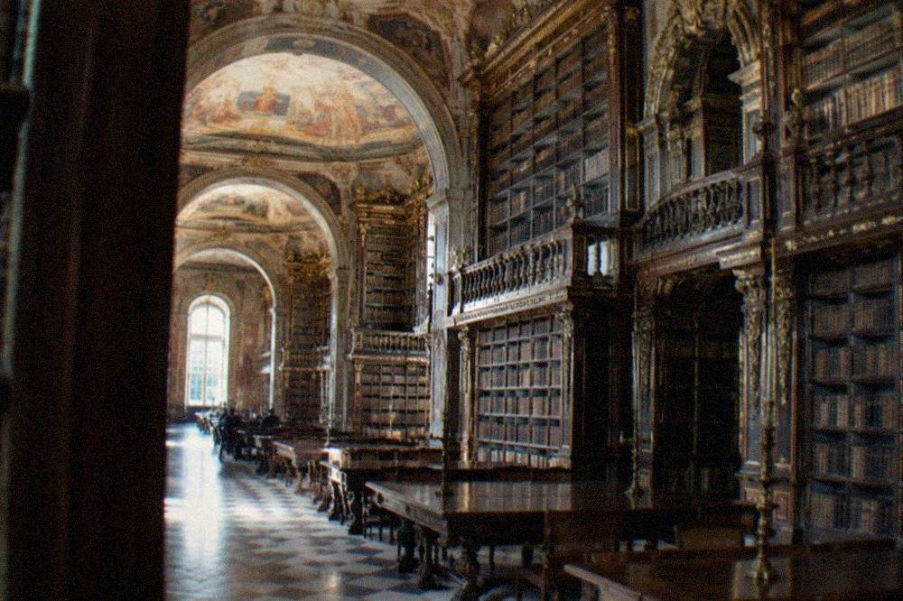 The baroque interior of the Joanina Library with tall wooden bookshelves and painted ceilings.