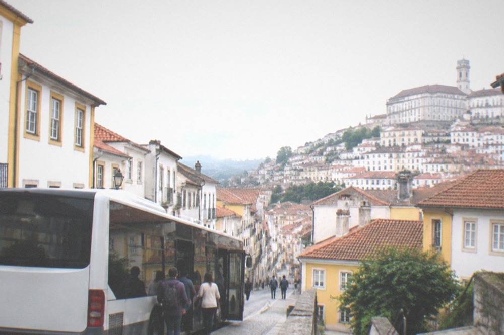 A city bus stopped on a narrow street in central Coimbra with passengers boarding.