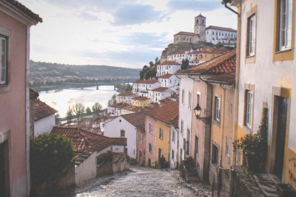 Cobblestone lane in Coimbra's old town with pastel painted houses and a view toward the river