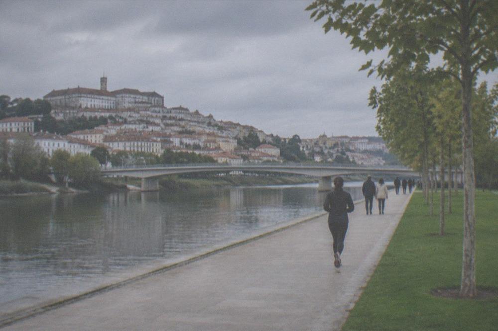 Visitors walking along the Mondego riverbank park with the old town rising on the far bank