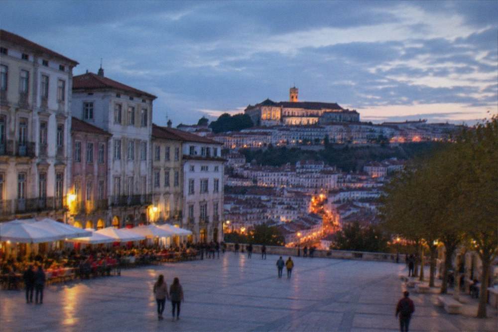 Evening lights of Coimbra's Baixa downtown streets with the university hill rising behind