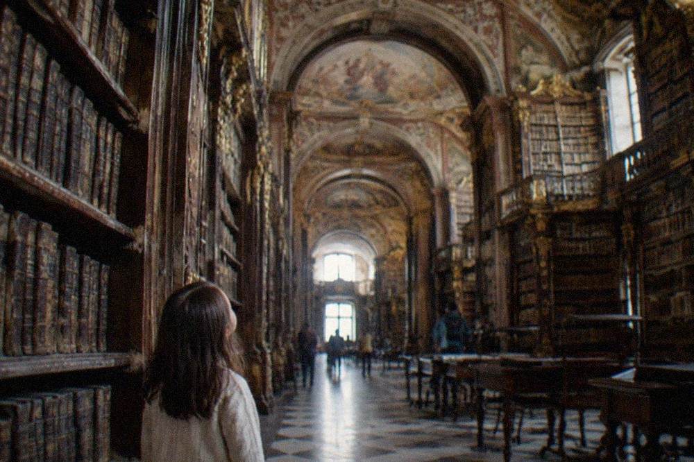 A child looking at the painted ceilings and gilded bookshelves inside a baroque library hall