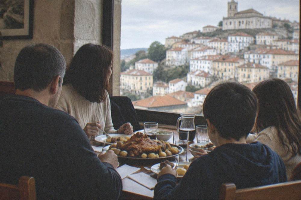 A family sharing a platter of roast pork and potatoes at a wooden table in a small restaurant
